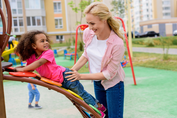 sorrindo mãe brincando com a filha de raça mista no playground
  - Foto, Imagem
