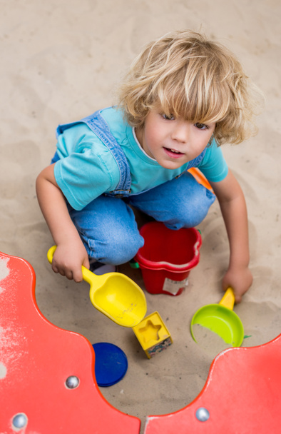 high angle view of little boy playing with plastic scoops, molds and bucket in sandbox at playgorund  - 写真・画像
