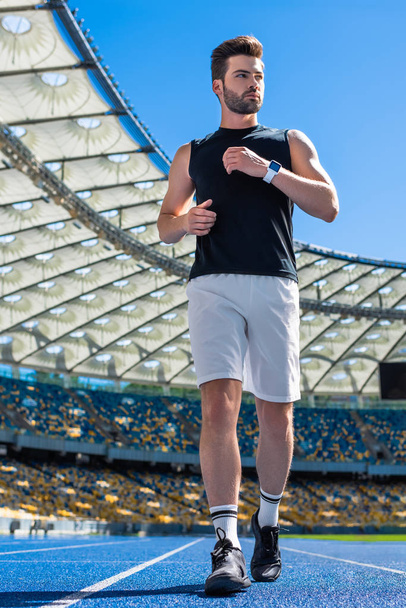 bottom view of fit young man exercising on running track at sports stadium - Фото, изображение