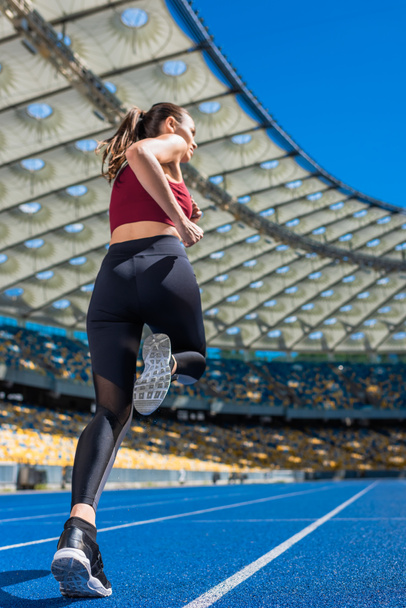 vista inferior de la joven deportiva corriendo en pista en el estadio deportivo
 - Foto, Imagen