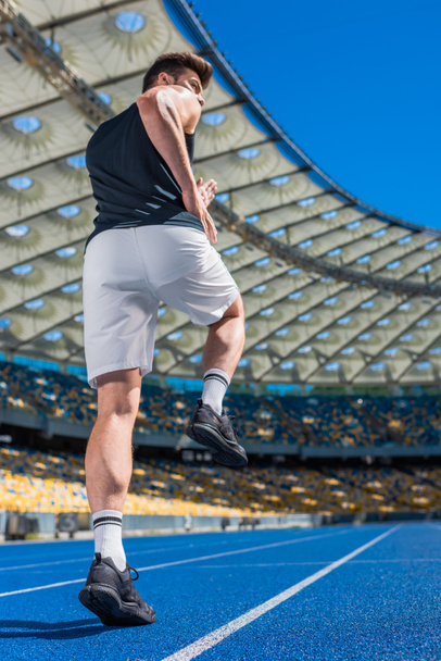 vista trasera del atlético joven que hace ejercicio en pista de atletismo en el estadio deportivo
 - Foto, Imagen