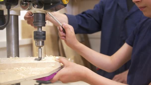 Adolescente chico perfora un agujero en un tablón de madera utilizando equipo industrial en taller de carpintería
 - Metraje, vídeo