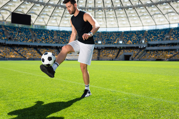 atletische jonge voetballer stuiterende bal op been bij sportstadion - Foto, afbeelding