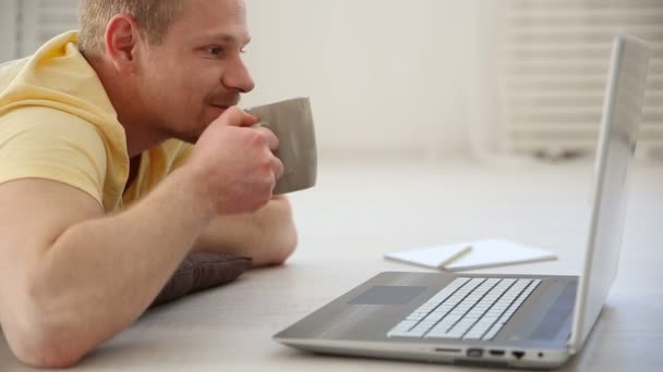 eine Pause in der Arbeit eines freien Mitarbeiters - ein Mann, der mit Kollegen in einem Videochat auf einem Laptop auf dem Boden spricht und Kaffee trinkt - Filmmaterial, Video