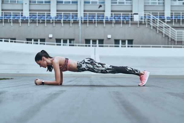 beautiful young woman in sports clothing keeping plank position while exercising outdoors - 写真・画像