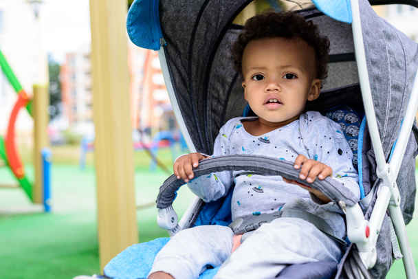 selective focus of african american toddler sitting in baby carriage at playgorund - Foto, Imagem