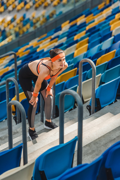 υψηλή γωνία άποψη κουρασμένος νεαρή γυναίκα χαλαρώνοντας στις σκάλες στο αθλητικό στάδιο - Φωτογραφία, εικόνα