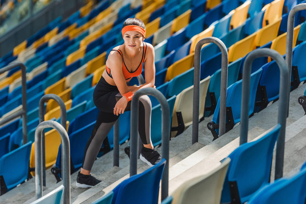 Blick aus der Vogelperspektive: Erschöpfte, fitte Frau entspannt sich auf Treppe im Sportstadion - Foto, Bild