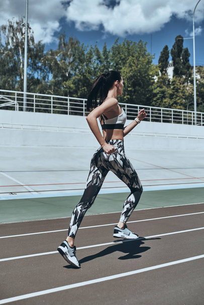 full length of brunette woman in sports clothing running on track stadium  - Фото, зображення