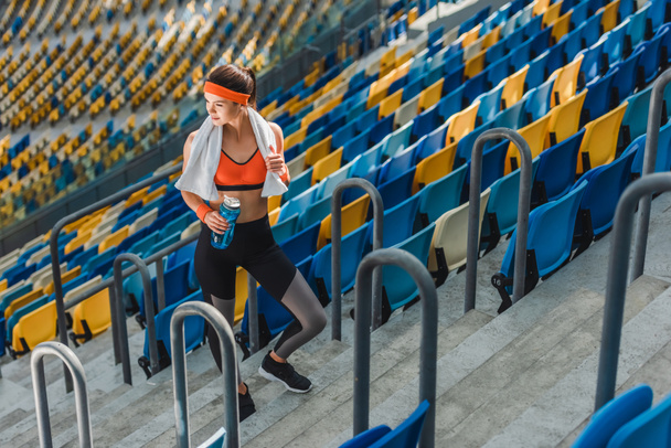 high angle view of beautiful young woman with water bottle and towel at sports stadium - Foto, immagini