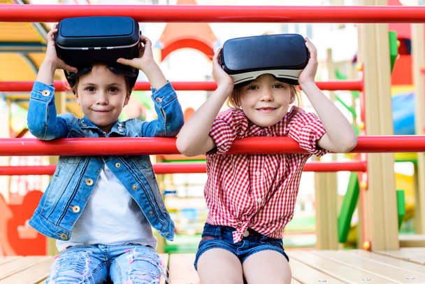 αξιολάτρευτο μικρό παιδιά απογείωση κάσκες εικονικής πραγματικότητας στην παιδική χαρά  - Φωτογραφία, εικόνα
