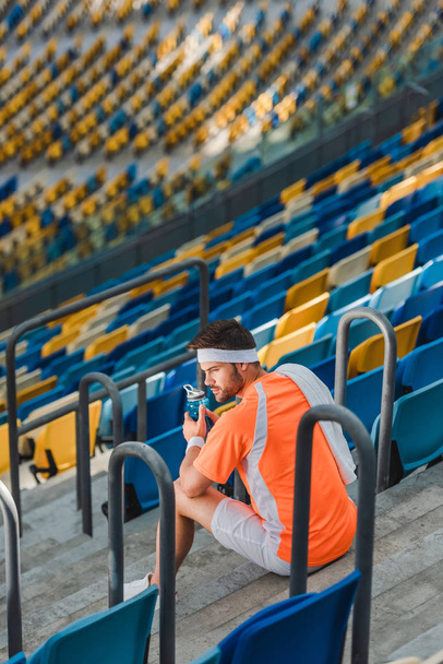 fatigué jeune sportif assis sur les escaliers au stade de sport avec bouteille d'eau
 - Photo, image