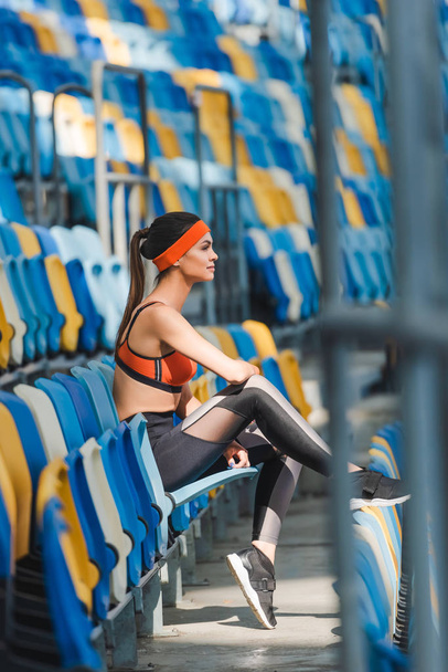 вид сбоку привлекательной молодой женщины, сидящей на трибунах на спортивном стадионе
 - Фото, изображение