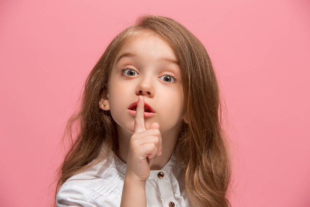 The young teen girl whispering a secret behind her hand over pink background - Foto, Imagen