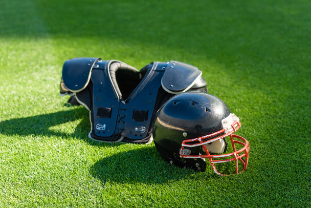 american football helmet with chest protection lying on green grass - Foto, afbeelding
