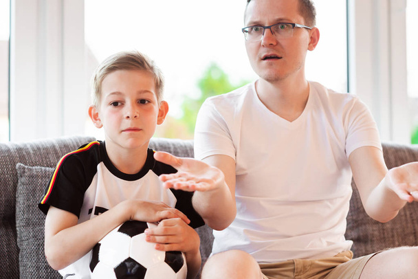 Young father and his son watching world soccer championship with ball on the sofa - Foto, afbeelding