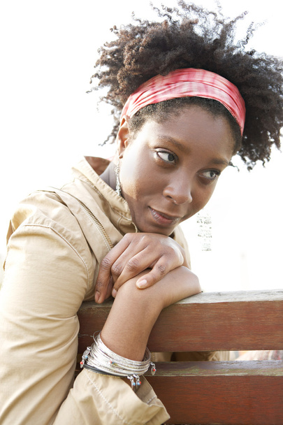 Young attractive african american woman being thoughtful while sitting on a bench in a city park. - Фото, изображение