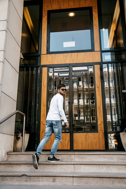 A young man travels through the streets of the city. Boy in sunglasses Stylish man near the building. The man sits on a whip. Beard and hair in a stylish guy. Senior student after studying. - Foto, Bild