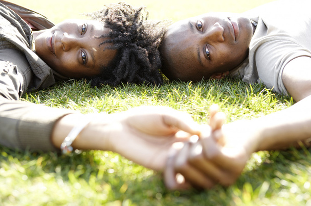 Close up portrait of a young african american couple laying down on green grass in the city - Photo, Image