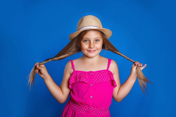 Portrait of young cute girl in pink dress and hat having fun on blue background . Summer vacation and travel concept - Valokuva, kuva