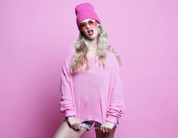 Stylish fashion portrait of trendy casual young woman in pink pulover and hat, posing over pink background. - Foto, Imagem