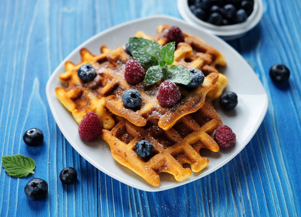 Belgian waffles with blueberries, raspberries and powdered sugar on wooden table. - Foto, Imagen
