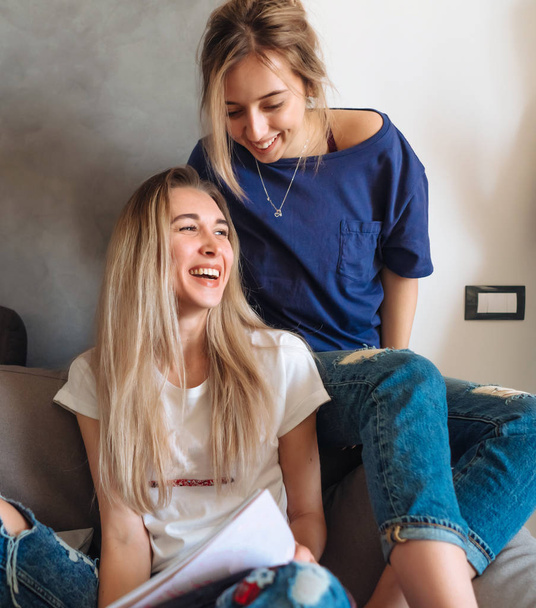 Две молодые девушки на диване смотрят журнал
 - Фото, изображение