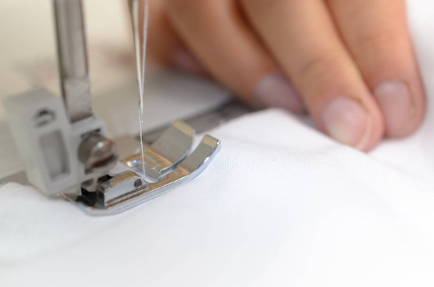 Manos costureras con material blanco detrás de la máquina de coser
. - Foto, Imagen