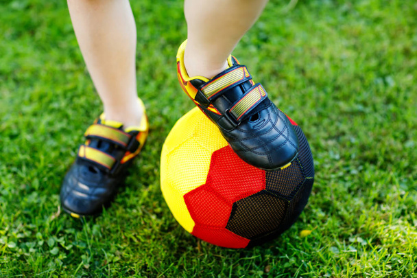 El primer plano de los pies del chiquitín con el fútbol y los zapatos de fútbol en los colores alemanes públicos - negro, dorado y rojo. Mundo o Europa concepto de copa
. - Foto, Imagen