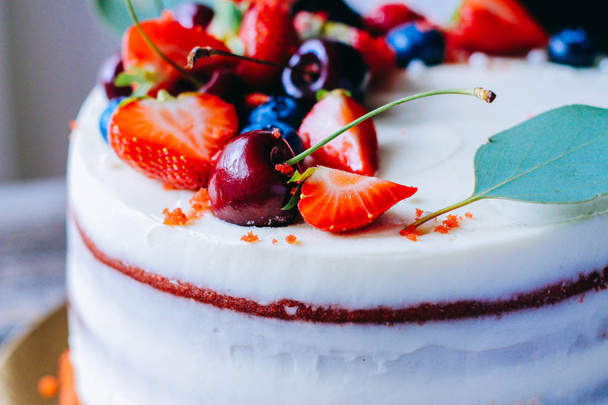 Красный бархатный торт с ягодным украшением из клубники, черники, вишни и эвкалипта на деревянном фоне
 - Фото, изображение