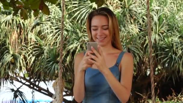 Αργή κίνηση μοντέλο κορίτσι που χρησιμοποιούν Internet στο smartphone χαλαρώνοντας στον κήπο - Πλάνα, βίντεο