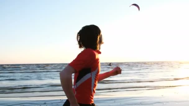 Okyanus gün batımında koşan adam ve zafer ellerini yukarı yükseltir ve bitirmek kitesurfers arka plan üzerinde atlama - Video, Çekim