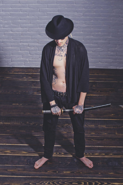 Warrior in black hat and open clothes showing tattooed torso - Foto, Imagen
