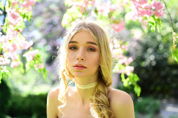Charming young blond lady with long curled hair in floral garden. Pretty girl with lace strip on her neck enjoying delicate fragrance of blooming flowers, retro style. Tenderness of youth concept - Foto, afbeelding