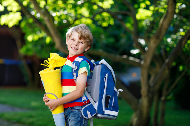 kis gyerek fiú iskola táska, iskola, iskola kúp ajándékokkal holding első napján - Fotó, kép