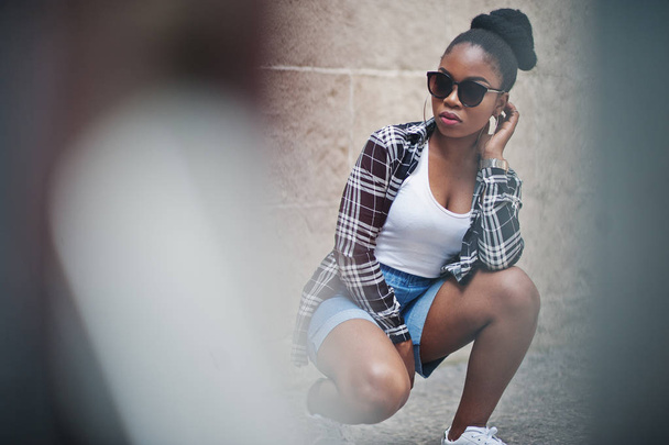 Hip hop african american girl on sunglasses and jeans shorts. Casual street fashion portrait of black woman. - Фото, зображення