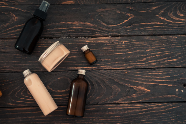 Bottles with spa cosmetic products from above on dark brown wood table. Beauty blogger, salon treatments concept. Minimalism, copyspace - Photo, Image
