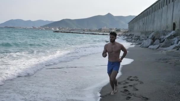Young man exercising, jogging and running on beach - 映像、動画