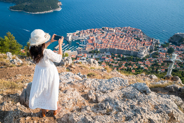 Viajero tomando fotografías del casco antiguo de Dubrovnik con teléfono móvil desde la vista aérea. El casco antiguo de Dubrovnik fue declarado Patrimonio de la Humanidad por la UNESCO en 1979
. - Foto, Imagen