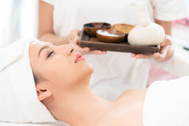 Uvolněná žena leží na posteli spa připravené pro lázně masáž terapeut drží lázeňské léčby v pozadí. Luxusní wellness, stres úlevu a omlazení koncept. - Fotografie, Obrázek