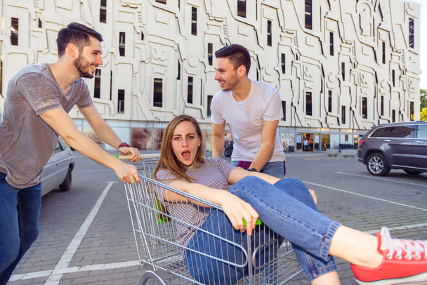 Retrato de comprimento total de um jovem empurrando uma mulher em um carrinho de compras
 - Foto, Imagem