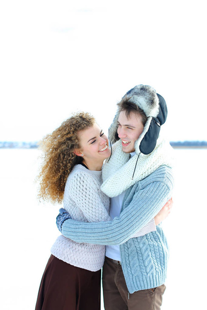 Girl hugging boy wearing winter hat and mittens in winter background. - Foto, imagen
