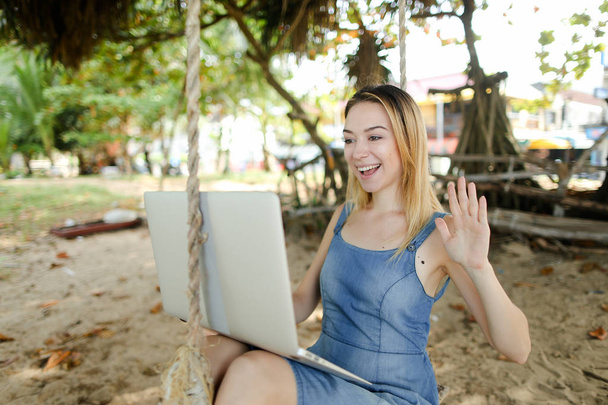 Jeune fille faire appel vidéo par ordinateur portable et équitation sur swing sur le sable
. - Photo, image