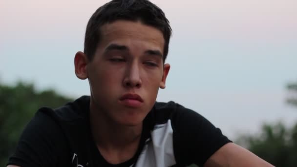 Έφηβος αγόρι κάθεται μόνος ψάχνει λυπημένος ή ανησυχούν. Αποθαρρυμένος αναστατωμένος νεαρό άνδρα συνεδρίαση στο ηλιοβασίλεμα. Η πόλη το βράδυ - Πλάνα, βίντεο
