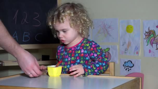 Рука дає милий маленька дівчинка йогурт і хліб і малюк дитина починає їсти
 - Кадри, відео