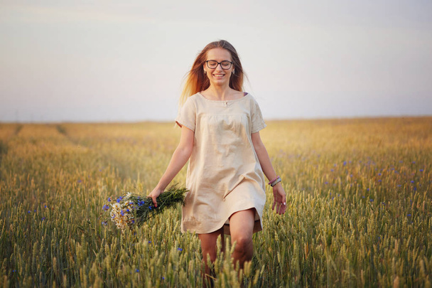 girl with flowers walking on a grain field - Foto, Imagen