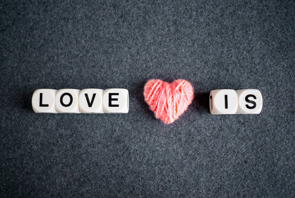 Liebe ist ein Textwort aus weißen Plastikblöcken und rosa Fadenherzen auf grauem Filzhintergrund. Liebe, Romantik, Valentinstag-Konzept - Foto, Bild
