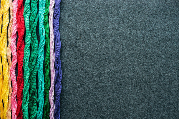 Яркие разноцветные нити нитей вышивки. Кожа из разноцветных вышитых ниток на темном войлочном полотне. Шитье ручной работы - Фото, изображение