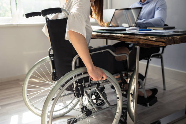 Disabled Businesswoman Sitting On Wheelchair With Laptop Over Desk - Foto, afbeelding