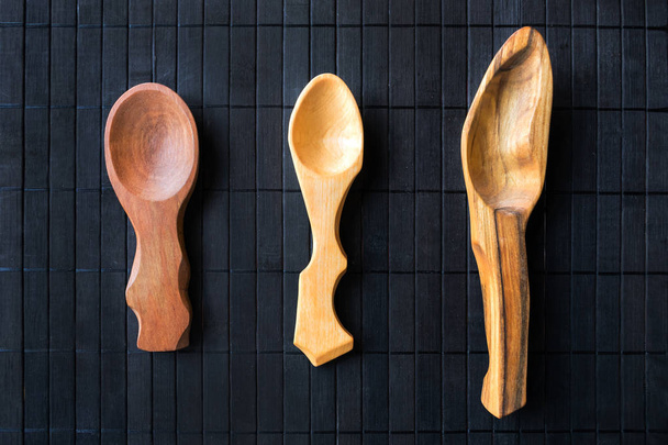 3 three empty handmade wooden spoons from different wood and different sizes on a black wooden background. Beautiful homemade spoons in a rustic style. Wood carving craft - 写真・画像